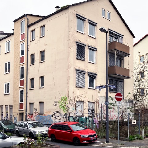 Mehrstöckiges Wohnhaus in einem Wohngebiet mit Graffiti an der Fassade, auf der Straße parken mehrere Autos.