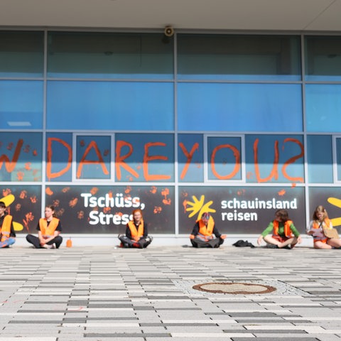 Sechs Mitglieder der Gruppierung "Letzte Generation" sitzen vor dem Flughafen Kassel-Calden vor dem Aufgesprühten Shriftzug "How Dare You?"