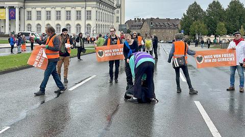 Menschen mit orangfarbenen Bannern - Aufschrift "Weg von Fossil-hin zu gerecht" - stehen verteilt auf einer mehrspurigen Straße mitten auf der Fahrbahn.