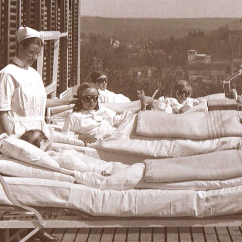 Historische Schwarz-Weiß-Aufnahme von Kindern, die in Krankenbetten auf einem Balkon liegen