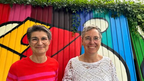 Gudrun Lang und Birgit Elbracht lächeln vor einem Graffitti in die Kamera