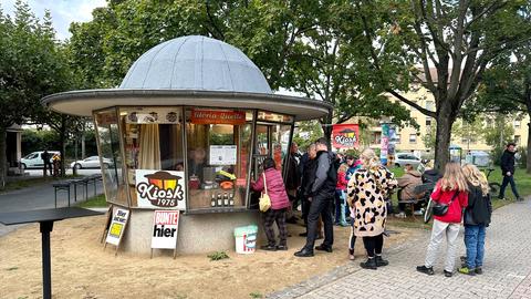 Am runden Kiosk 1975 im 70er-Jahre-Retrostil steht eine Schlange von Gästen an, um sich Getränke und Naschtüten zu kaufen.