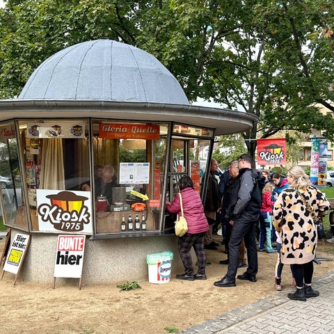 Am runden historischen Kioskhäuschen steht eine Schlange von Menschen an.