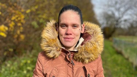 Eine Frau Ende 20 mit schwarzen Haaren und Piercings im Gesicht steht in einer dicken Winterjacke draußen auf einem Feldweg