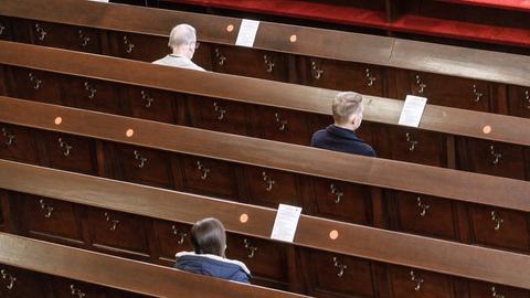 Drei Gläubige sitzen mit Sicherheitsabstand im Gottesdienst.