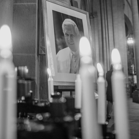 Portraitbild von Papst Benedikt XVI. steht zwischen Kerzen in einer Kirche.