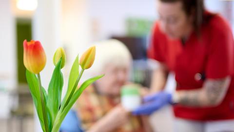 Eine Pflegekraft unterstützt eine Seniorin beim Frühstück