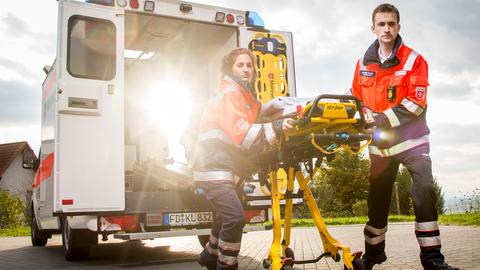 Eine Sanitäterin und ein Sanitäter ziehen eine Rettungstrage aus einem Einsatzfahrzeug.