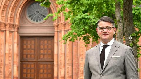 Boris Rhein steht in einem grauen Anzug vor dem Eingangsportal der Wiesbadener Marktkirche