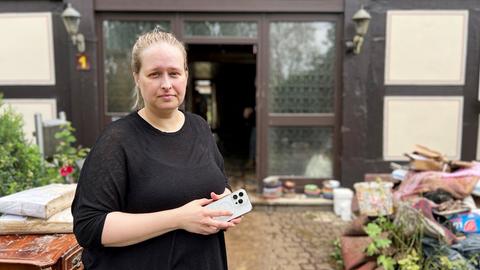 eine Frau steht vor ihrem Haus und schaut in die Kamera