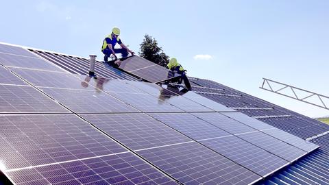 Zwei Männer mit gelben Helmen arbeiten auf einer großen Dachfläche mit vielen Solarpanelen.