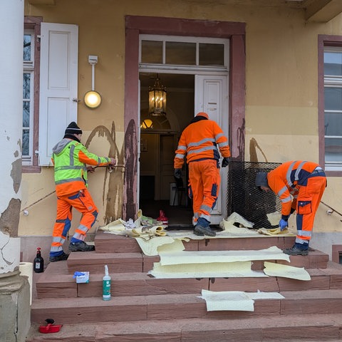 Mitarbeiter der Stadt reinigen den Eingang des Ordnungsamts, nachdem Unbekannte die Fassade und die Tür mit Öl beschmiert haben. 