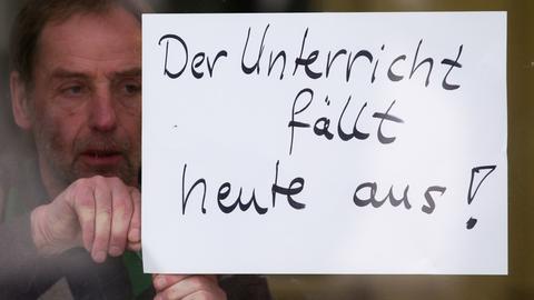 Mann hängt Schild mit Aufschrift "Der Unterricht fällt heute aus" auf