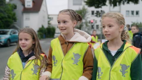 Schülerinnen mit gelben Westen vor Schule