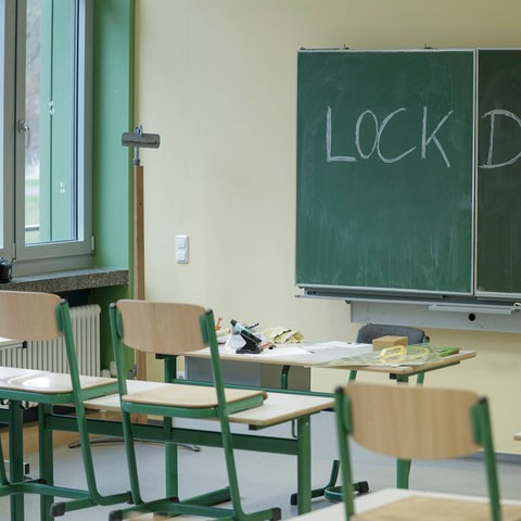 Die Stühle im Klassenraum sind hochgestellt, auf der Tafel steht mit Kreide das Wort "Lockdown".