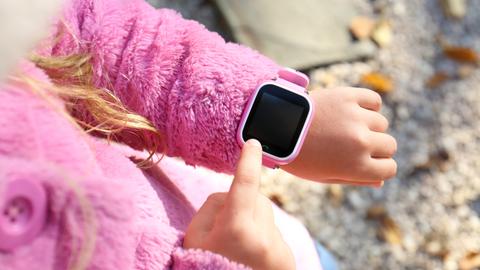 Mädchen - von hinten fotografiert - in rosa Flauschjacke zeigt auf die rosa Smartwatch an ihrem Arm