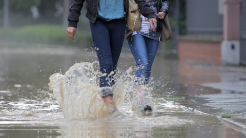 Zwei Personen laufen durch Wasser, das auf einer Straße steht. 