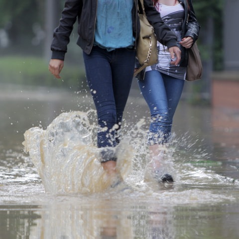 Zwei Personen laufen durch Wasser, das auf einer Straße steht. 