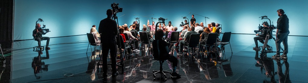 Fast 40 Menschen sitzen in einem dunklen TV-Studio.