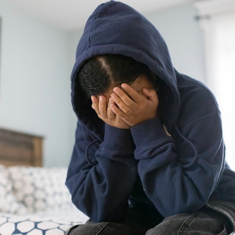 Ein Mädchen sitzt anscheinend verzweifelt in einem Zimmer und vergräbt das Gesicht in den Händen