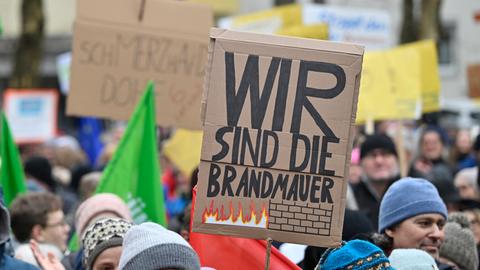 Menschen protestieren gegen rechts, ein Teilnehmer hält ein Pappschild mit der Aufschrift: "Wir sind die Brandmauer".