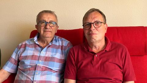 Zwei ältere Männer sitzen auf einer roten Couch.