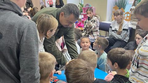 Eine Gruppe von Kindern sitzt in einem Zimmer, Askold Kvyatkovskiy zeigt ihnen etwas.