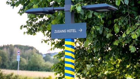 Nahaufnahme eines Schildes mit dem Wort "Hotel". Die Stange, an welcher das Schild befestigt ist, ist abwechselnd mit blauem und gelbem Band umklebt. 