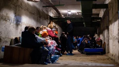 Mehrere Familien sitzen in einem dunklen Gang mit Betonwänden in einem Bunker in Mariupol