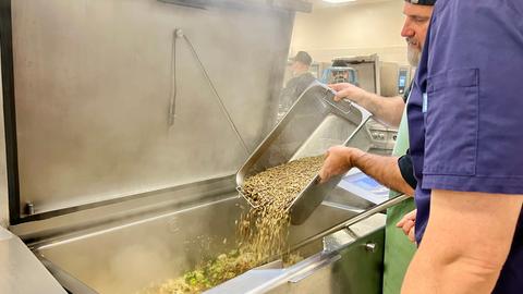 Koch kippt braune Schnitze in einen großen Gastro-Bräter