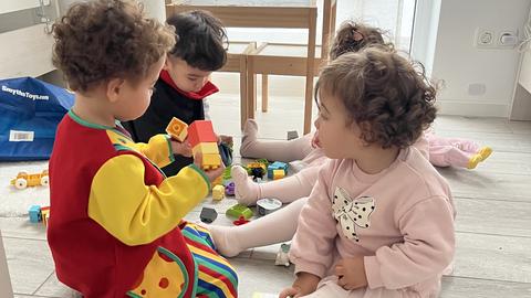 Die vier kleinen Kinder sitzen auf dem Boden im Kinderzimmer und spielen.