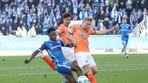 Andreas Müller (im orangenen Lilien-Trikot) blockt einen Schuss von Lubambo Musonda (blaues Magdeburg-Trikot)