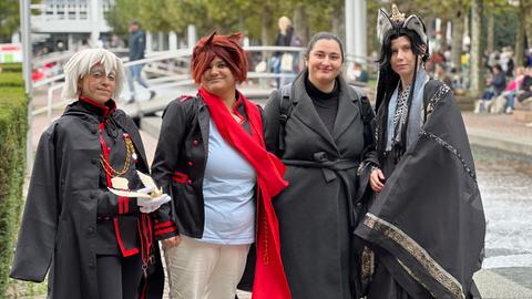 Das Bild zeigt drei Cosplayer auf der Buchmesse 2024. Sie sind unter anderem mit Katzenohren und Perücken verkleidet. Eine vierte Person in der Mitte trägt Straßenkleidung.