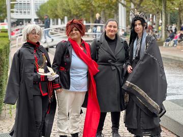 Das Bild zeigt drei Cosplayer auf der Buchmesse 2024. Sie sind unter anderem mit Katzenohren und Perücken verkleidet. Eine vierte Person in der Mitte trägt Straßenkleidung.