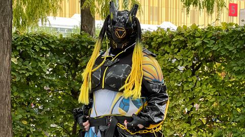 Das Bild zeigt einen Cosplayer auf der Buchmesse 2024. Er trägt eine schwarze Gesichtsmaske mit Hörnern und eine gelbe Langhaarperücke, dazu eine Art Brustpanzer.