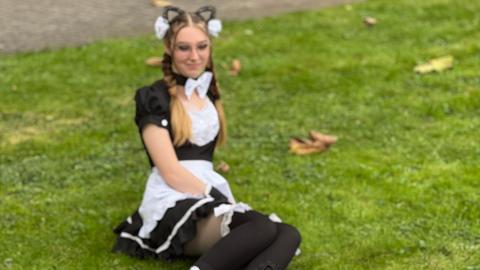 Das Bild zeigt Cosplayer auf der Buchmesse 2024. Eine als Katze verkleidete Frau posiert auf einer Wiese liegend für eine weitere Frau, die vor ihr kniet und die Kamera auf sie gerichtet hat.