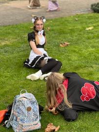 Das Bild zeigt Cosplayer auf der Buchmesse 2024. Eine als Katze verkleidete Frau posiert auf einer Wiese liegend für eine weitere Frau, die vor ihr kniet und die Kamera auf sie gerichtet hat.