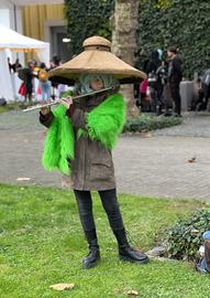 Das Foto zeigt eine Cosplayerin auf der Buchmesse 2024. Sie trägt einen übermäßig großen Strohhut und hält eine Querflöte vor den Mund.