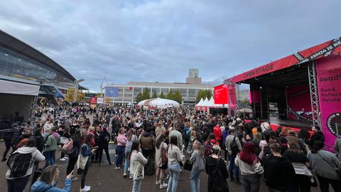 Das Bild zeigt die Agora der Frakfurter Buchmesse. Viele Menschen haben sich vor einer Open-Stage-Bühne auf dem Außengelände versammelt.