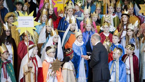 Kinder als Sternsinger verkleidet auf einer Treppe, ein Mann im Anzug schüttelt einem Kind die Hand