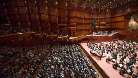 Das Bild zeigt den Großen Saal der Alten Oper Frankfurt. Auf der Bühne steht ein Orchester, die Publikumsränge sind gefüllt.