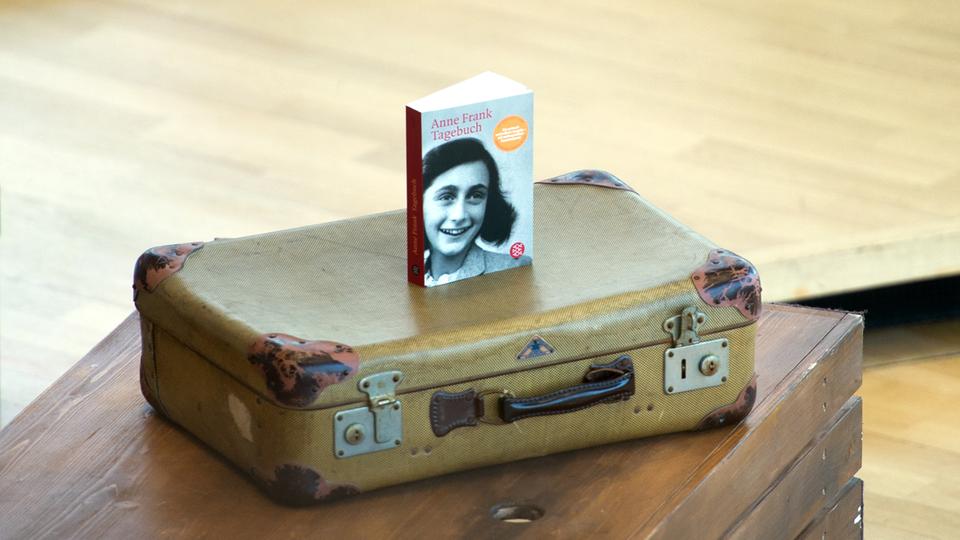 Ein Buch "Anne Frank Tagebuch" steht auf einer alten Schülerbank