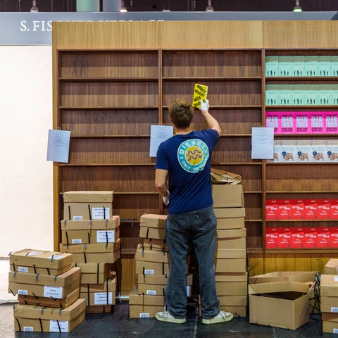 Das Bild zeigt einen Mann im T-Shirt von hinten. Er räumt Bücher in ein Regal auf der Frankfurter Buchmesse.