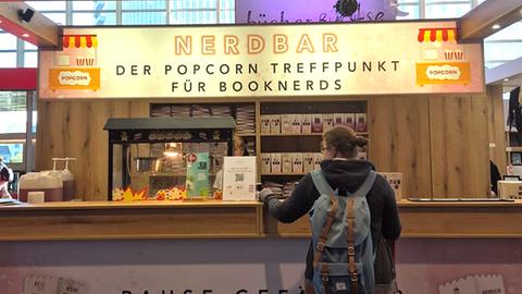 Eine Frau steht an einem Stand "Nerdbar. Popcorntreffpunkt für Booknerds"