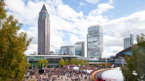 Aus der Ferne Blick auf die "Agora" auf das Messegelände mit Messeturm und Hochhaus. Davor viele Menschen vor einer Bühne.