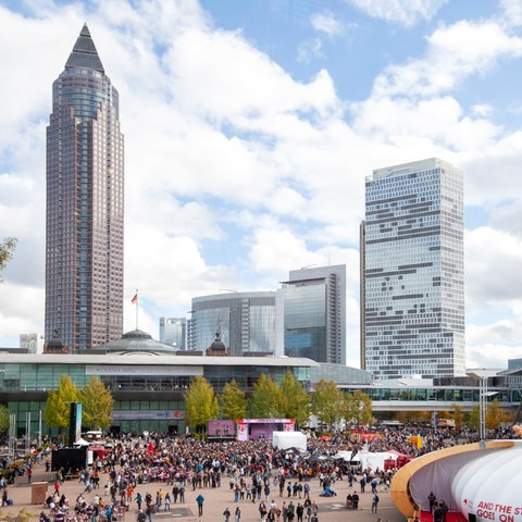 Aus der Ferne Blick auf die "Agora" auf das Messegelände mit Messeturm und Hochhaus. Davor viele Menschen vor einer Bühne.