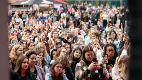 Besucherinnen halten Handy in ihren Händen. Sie stehen vor einer Outdoor-Bühne. 