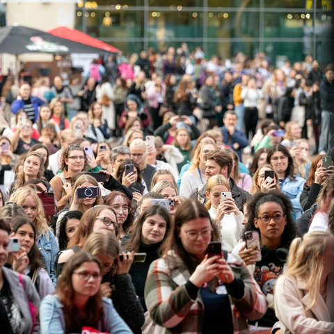 Besucherinnen halten Handy in ihren Händen. Sie stehen vor einer Outdoor-Bühne. 