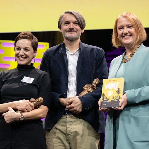 Sasa Stanisic und die Illustratorin Regina Kehn (links) nehmen den Jugendliteraturpreis für ihr Kinderbuch "Wolf" von Bundesfamilienministerin Lisa Paus (Grüne) entgegen. 