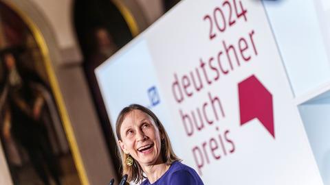 Frau lacht, hinter ihr steht ein Schild mit der Aufschrift "Deutscher Buchpreis"